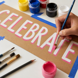 Painting opaque white and tropical pink lettering on a brown kraft paper banner